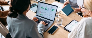 From above photo of unrecognizable team of six multi-ethnic employee reading and typing business report on laptop computers and digital tablet while sitting together at office desk.