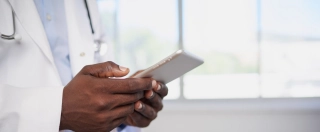 Close up of Black doctor entering patient information into digital tablet.