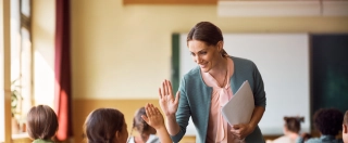 Happy elementary school teacher giving high-five to her student during class in the classroom.