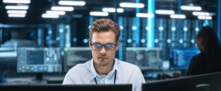 Focused system administrator or consultant looks at the screen and saves backup data in dark evening room workplace station indoors.