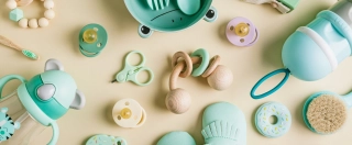 Baby care accessories and bootees. Newborn baby pacifier, teethers, nail scissors, hair brush, spoon and fork on a beige background. Wish list or shopping overview for pregnancy.