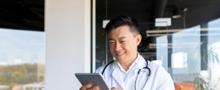 Cheerful and friendly Asian in a modern clinic, online video call, uses a tablet, to communicate with patients.