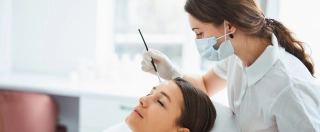 Concentrated skilled female beauty therapist spreading a cosmetic product over a young woman's forehead.