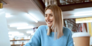Education, university and happy woman in library with laptop, research and books for school project or exam. Smile, internet and college phd student studying with technology and elearning on campus.