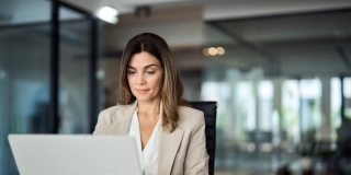 Busy mature middle aged professional business woman manager executive looking at laptop computer technology in office working on digital financial banking market sitting at desk. Copy space.