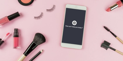 Set of make up brushes and cosmetics on pink background with a ChatGPT interface on a smartphone.